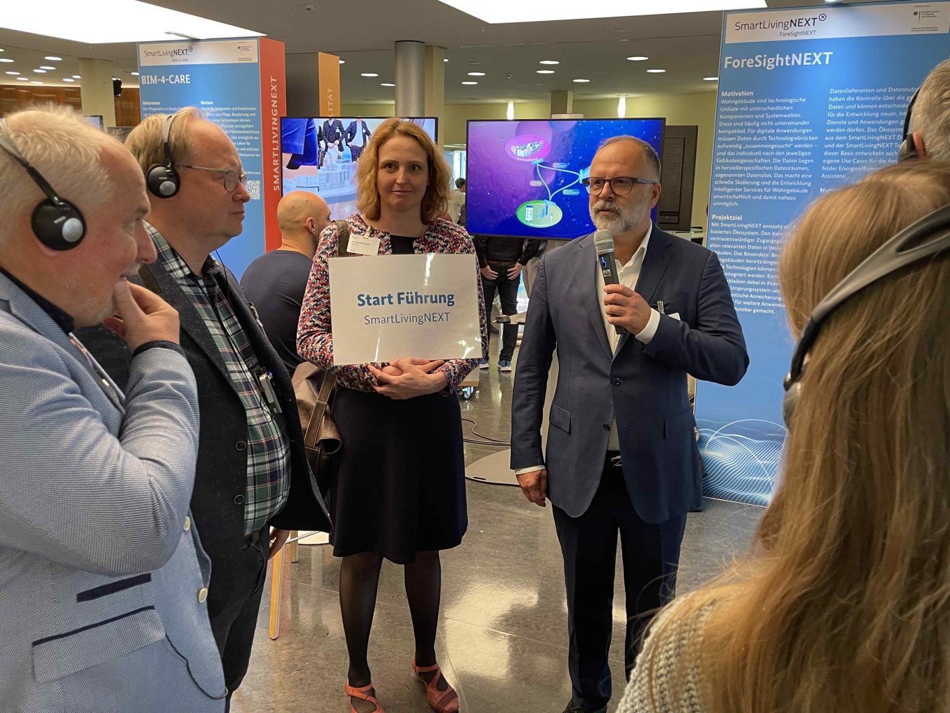 Auf den TddT wurden themenspezifische Führungen zu den Ausstellern organisiert. Marieke Rohde, VDI/VDE, führte Besucherinnen und Besucher u. a. zum Stand von SmartLivingNEXT. Michael Schidlack, Principial Researcher bei der Forschungsvereinigung Elektrotechnik (FE) beim ZVEI e. V. und Konsortialleitung im SmartLivingNEXT Leitprojekt, erläuterte den strategischen Ansatz und Mehrwerte des mittlerweile entstandenen Ökosystems. Foto: Maximilian Metzner